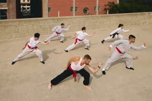 A group of Shaolin Wing Chun practitioners in traditional attire performing the 5 animals of Shaolin Kung Fu styles on a rooftop with an urban backdrop.