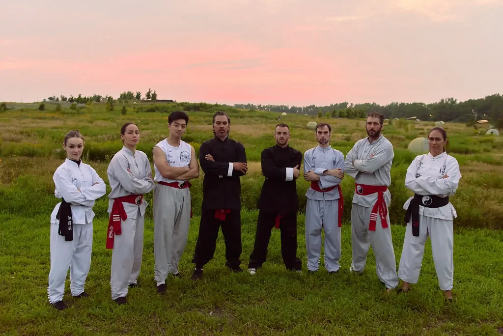 A group of Shaolin Wing Chun practitioners standing together in traditional martial arts attire, set against a scenic outdoor backdrop during sunset.