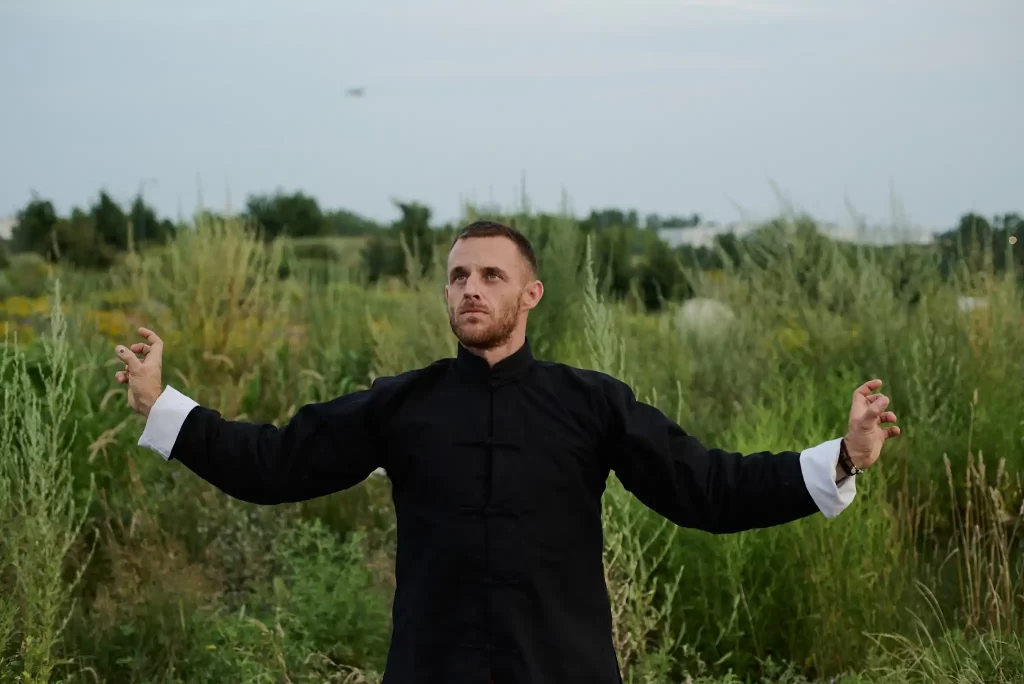 A Tai Chi practitioner from Shaolin Wing Chun in Montreal in a meditative stance with arms extended, wearing traditional black attire, set against a serene natural landscape.